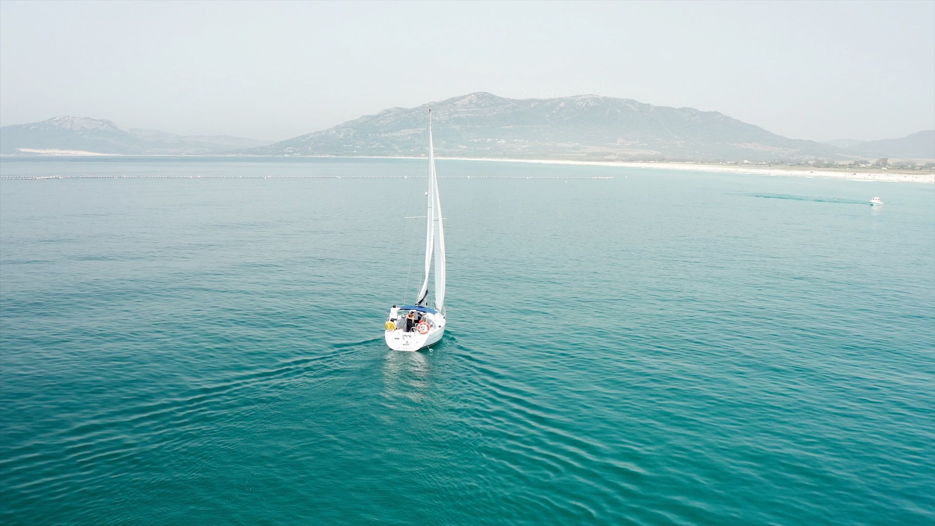 Vista aérea del velero YEMAYA navegando hacia la playa de Los Lances en Tarifa, con la sierra al fondo