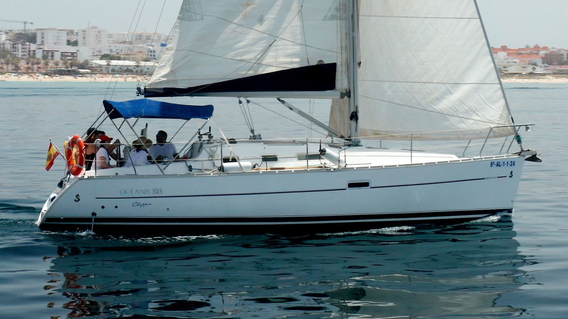 Grupo disfrutando a bordo del velero con el patrón al timón, bajo el bimini
