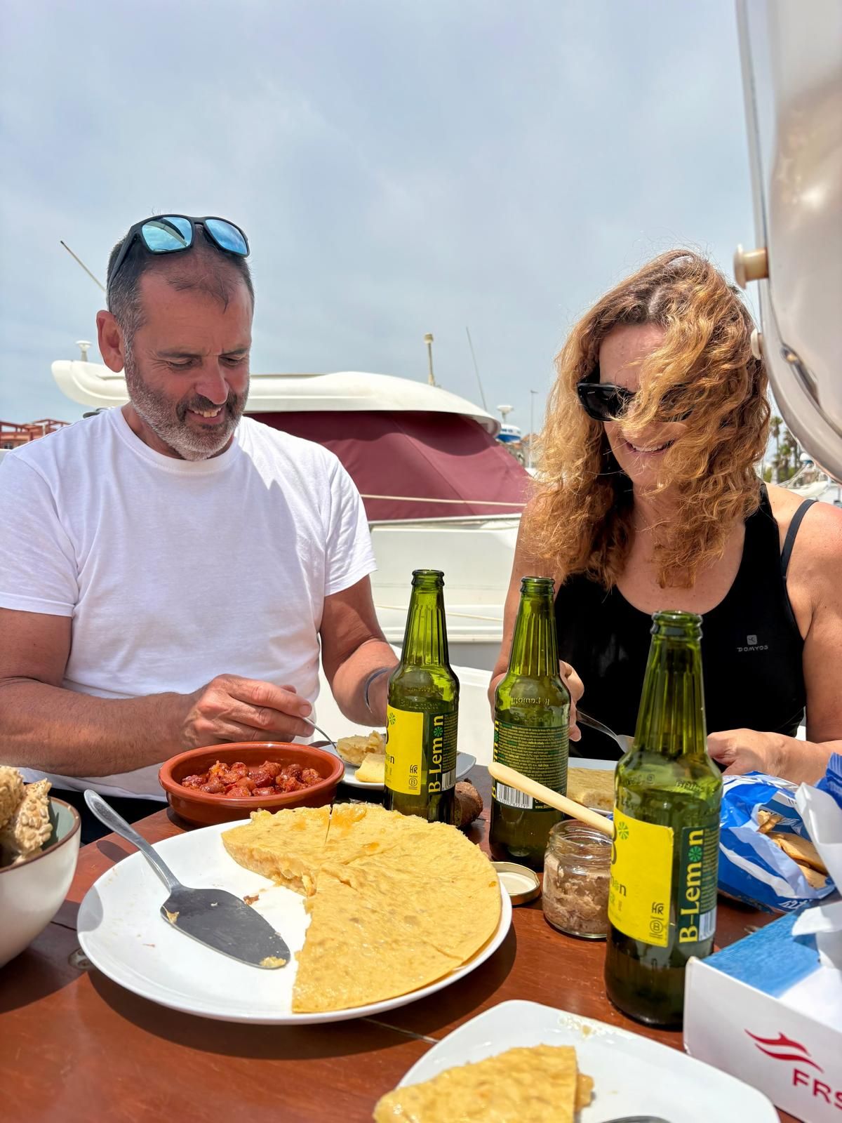 Una pareja disfruta de tortilla, tapas y cervezas frías a bordo del velero en el puerto de Tarifa