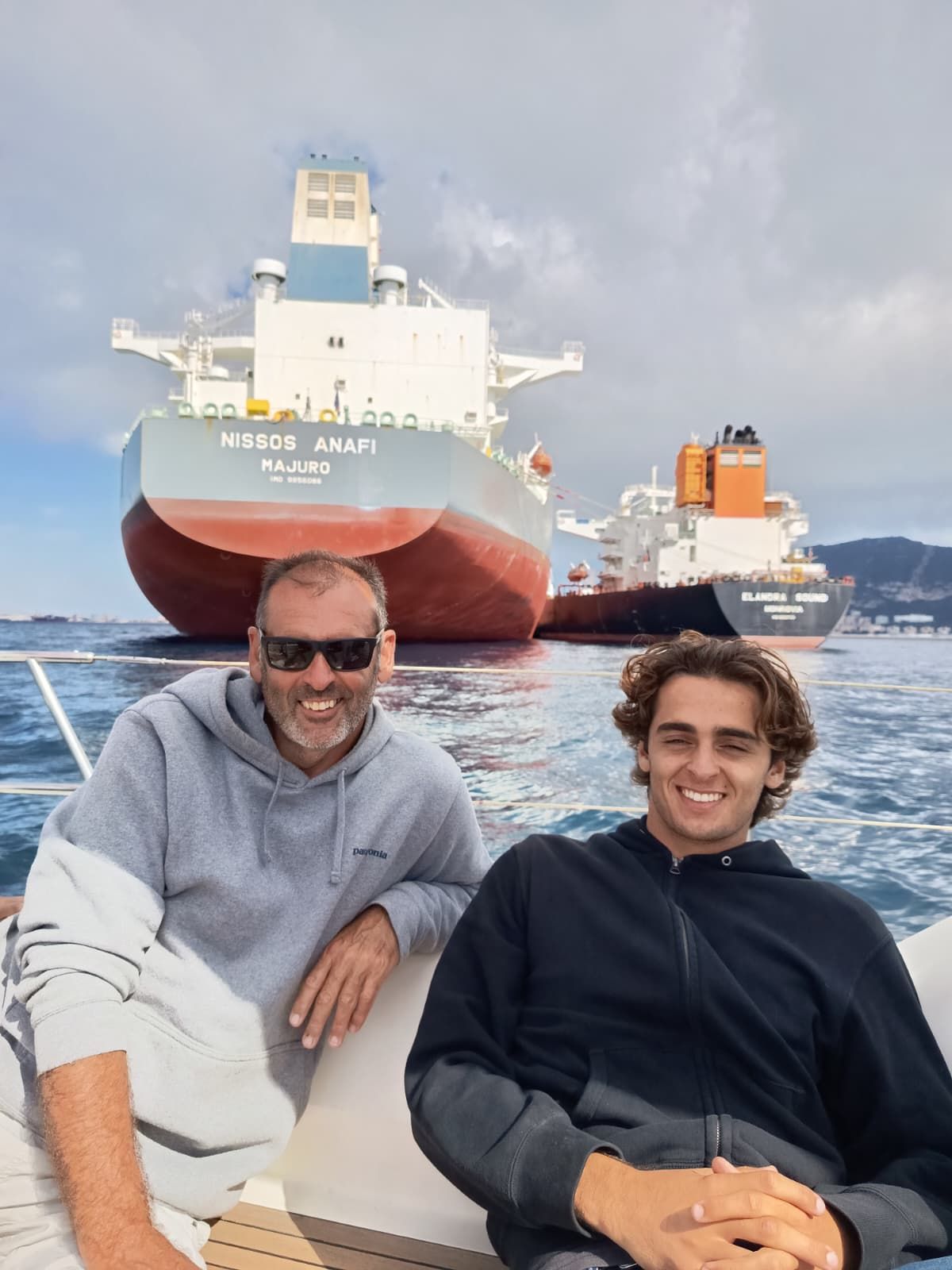 Dos pasajeros sonríen en cubierta con los grandes cargueros del Estrecho de Gibraltar y el Peñón al fondo